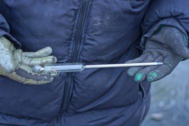 fingers holding an one old glass alcohol thermometer on an autumn street clipart