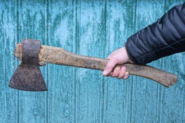 Güz sokağında yeşil duvara yaslanmış büyük gri kahverengi baltayı tutan siyah elbiseli bir el.