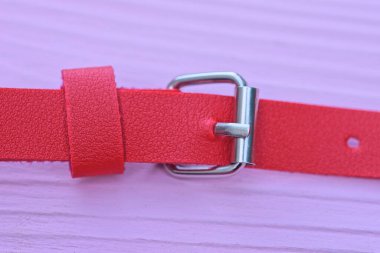 Pembe ahşap bir masanın üzerinde gri metal tokalı uzun deri bir kırmızı kayış var.