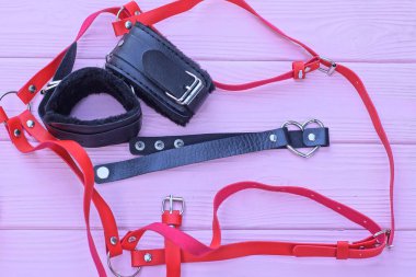 Oyun siyah deri kelepçeli, yakası kürklü, boynu kırmızı, omuz kemeri pembe, ahşap masada.