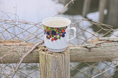 Renkli desenli bir beyaz seramik bardak sonbahar caddesinde gri ahşap çitin üzerinde duruyor.