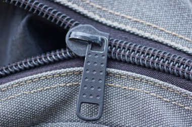 Büyük bir sırt çantasının gri kumaşında bir siyah metal fermuar.