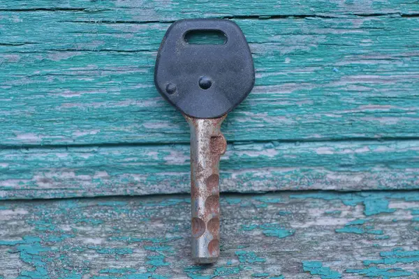 Siyah plastik saplı eski bir gri demir paslı kapı anahtarı yeşil ahşap masada yatıyor.