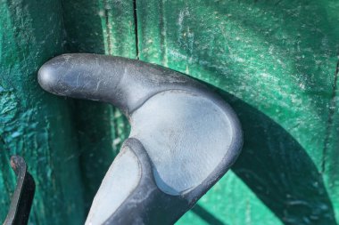 Motosikletin bir kısmı siyah metal bir gidonun parçası ve yeşil duvarda da plastik gri bir sapı var.