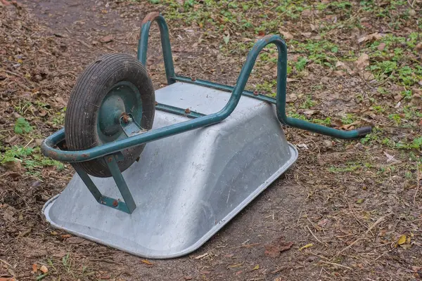 Büyük gri bir metal devrilmiş bir bahçe el arabası bir yaz bahçesinde yerde yatıyor.