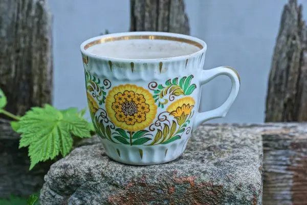 Renkli desenli bir beyaz seramik bardak, caddede gri bir direğin üzerinde duruyor.