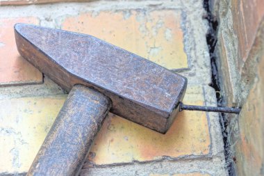 Büyük kahverengi bir demir çekiç paslı bir çiviyi sokaktan duvara çakıyor.