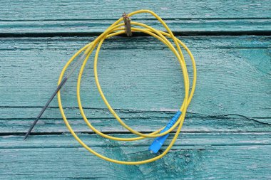 Bir yaz sokağında yeşil ahşap bir duvara asılı sarı bir tel çizik.