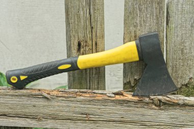 Kırsal sokaktaki gri ahşap çitlerin üzerinde siyah saplı büyük bir balta yatıyor.