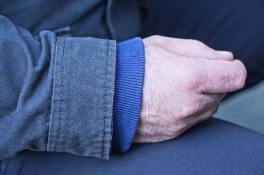 Bir elin mavi kollu süveter ve gri siyah ceketli caddede