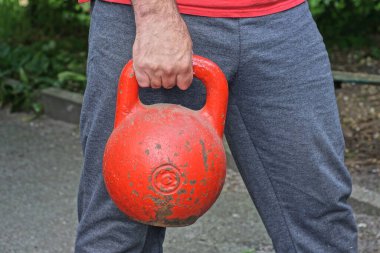 Bir erkek sporcunun eli yaz caddesinde büyük bir kırmızı demir spor ağırlığını kaldırıyor.