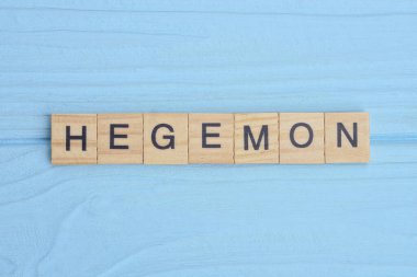 Sözcük hegemon ahşap gri harflerden yapılır mavi bir arka planda yatar