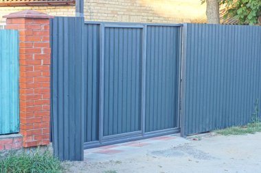 Gri asfalt bir yolun yakınındaki uzun demirden bir duvarda siyah metal bir kapı.