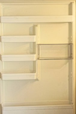 Mutfaktaki açık buzdolabının kapısında beyaz plastik raflar ve kutular var.