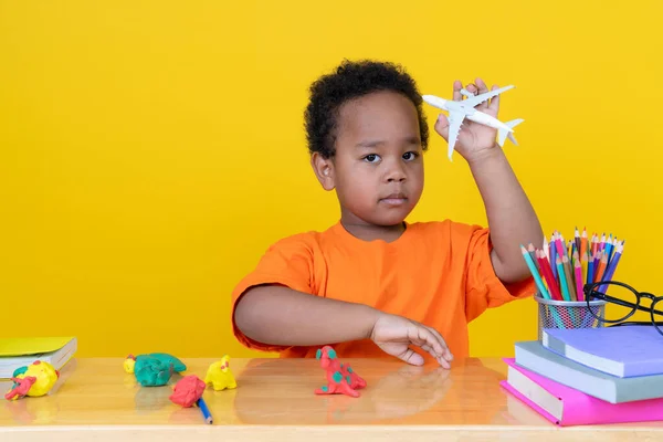 小男孩想象自己是个在黄色背景下玩玩具飞机的飞行员 — 图库照片