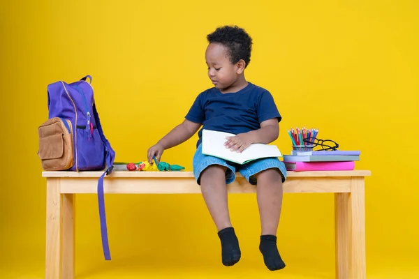 可爱的小男孩在黄色的背景上用铅笔在笔记本上写字 — 图库照片