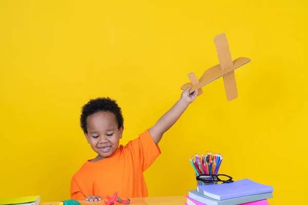 小男孩想象自己是个在黄色背景下玩玩具飞机的飞行员 — 图库照片