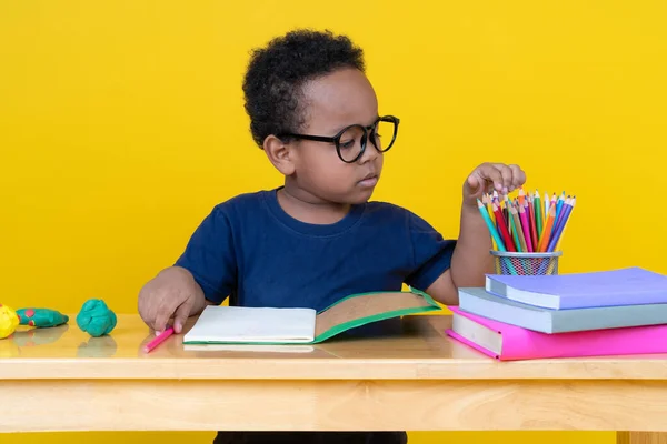 想像力を持つ小さな男の子黄色の背景に色鉛筆でテーブルの図面に座って — ストック写真