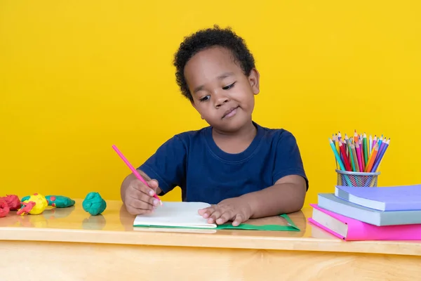 想像力を持つ小さな男の子黄色の背景に色鉛筆でテーブルの図面に座って — ストック写真