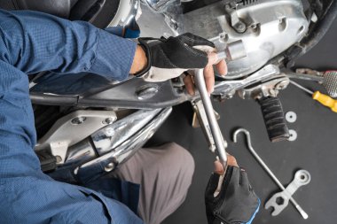Motosiklet tamircisi, insanlar motorsikleti tamir ediyor. Çalışmak için ingiliz anahtarı ve tornavida kullanıyorlar.