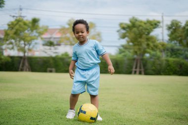 Güneşli bir günde parkta futbol topuyla gezen sevimli küçük çocuk eğlenmek için dışarı çıktı..