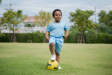 Güneşli bir günde parkta futbol topuyla gezen sevimli küçük çocuk eğlenmek için dışarı çıktı..