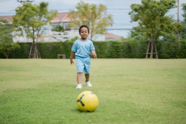 Güneşli bir günde parkta futbol topuyla gezen sevimli küçük çocuk eğlenmek için dışarı çıktı..