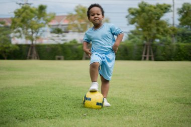Güneşli bir günde parkta futbol topuyla gezen sevimli küçük çocuk eğlenmek için dışarı çıktı..