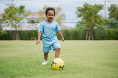 Güneşli bir günde parkta futbol topuyla gezen sevimli küçük çocuk eğlenmek için dışarı çıktı..