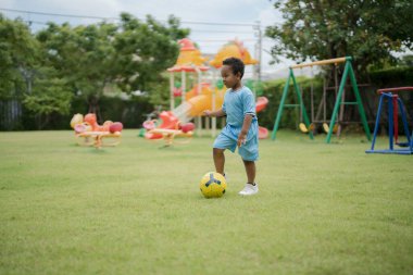 Güneşli bir günde parkta futbol topuyla gezen sevimli küçük çocuk eğlenmek için dışarı çıktı..