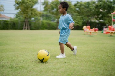 Güneşli bir günde parkta futbol topuyla gezen sevimli küçük çocuk eğlenmek için dışarı çıktı..