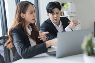 Ofisteki dizüstü bilgisayarları kullanarak masa başında oturan iş adamlarının modern bir çalışma alanında birlikte çalışırken yüzlerinde ciddi ve endişeli bir ifade vardı..