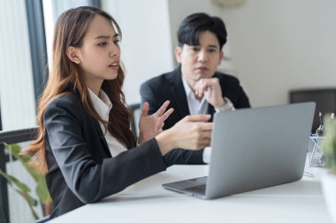 Ofisteki dizüstü bilgisayarları kullanarak masa başında oturan iş adamlarının modern bir çalışma alanında birlikte çalışırken yüzlerinde ciddi ve endişeli bir ifade vardı..