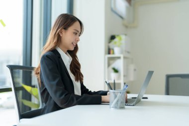 Modern bir ofiste iş bilgisi için dizüstü bilgisayarda çalışan bir iş kadını..