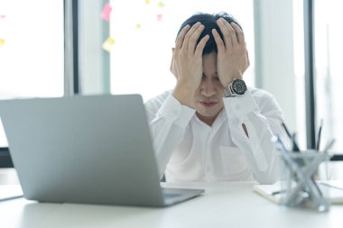 Genç işadamı masasında oturmuş bilgisayarından internete bakıyor. Ofiste stresli, endişeli ve mutsuz hissediyor..