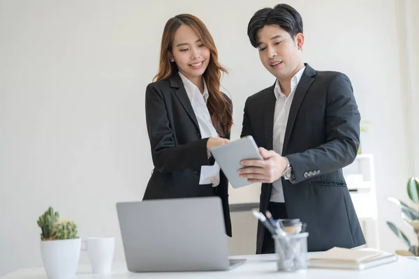 stock image Business people stand together at a desk talking on their laptops and notebooks in the office The two discussed the idea of running a business together in a modern workspace.