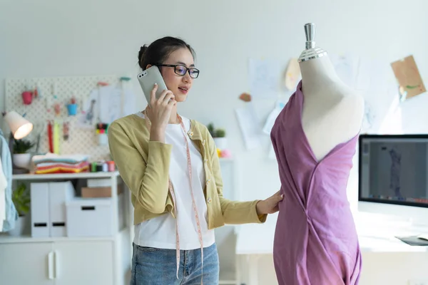 stock image Designer girl wearing glasses Talking on the phone and examining the design of the clothes on the mannequin