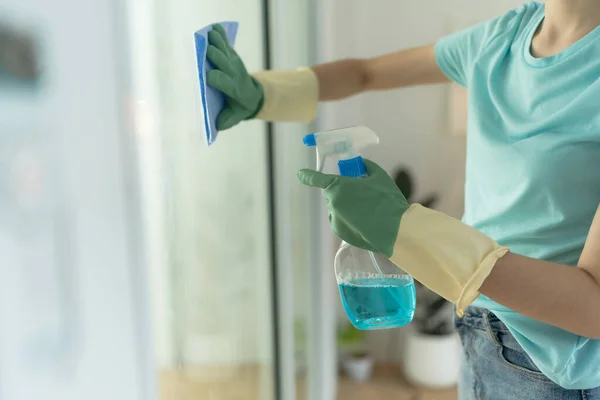 Female hand in green gloves cleaning door with blue rag and spray detergent house cleaning.