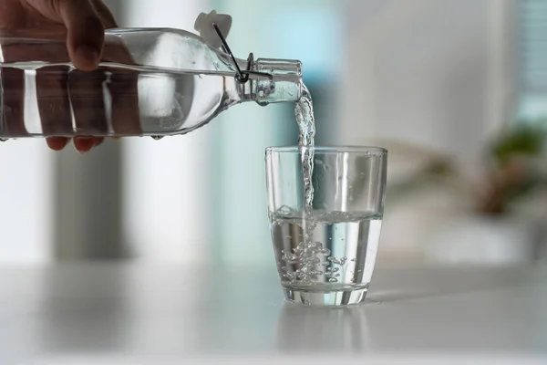 Pour the water from the water bottle into the glass at home.