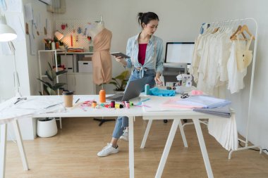Terzilik stüdyosunda tablete bakan kadın girişimci son teknoloji kullanarak yeni koleksiyonlar üreten bir tekstil tasarımcısı..