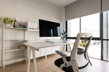 White table and chair with computer monitor and modern file cabinet in white home office interior