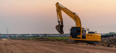 Excavator working on construction site at sunset background, Backhoe digs soil and gravel in countryside