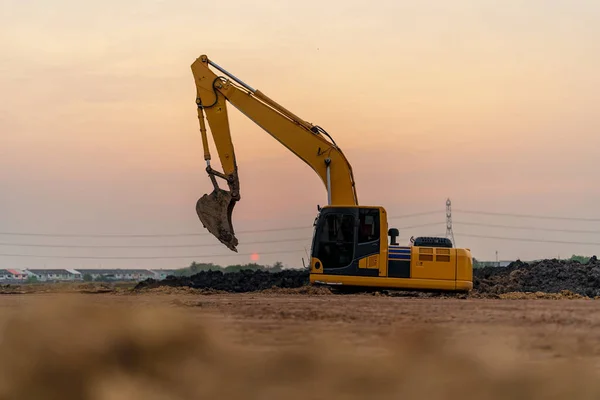 Excavator working on construction site at sunset background, Backhoe digs soil and gravel in countryside