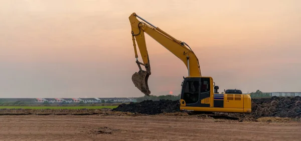 Excavator working on construction site at sunset background, Backhoe digs soil and gravel in countryside