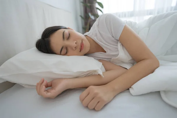 睡在舒适的白色卧室里的年轻女人让身体休息一下 图库图片