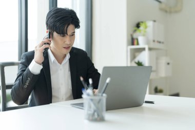 Genç işadamı telefonda iş hakkında konuşuyor ve ofisteki işin başarısını görmek için defteri açıyor..
