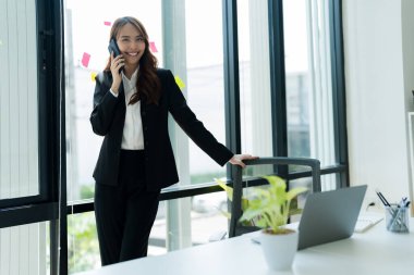 Happy young asian business woman wearing suit holding mobile phone.