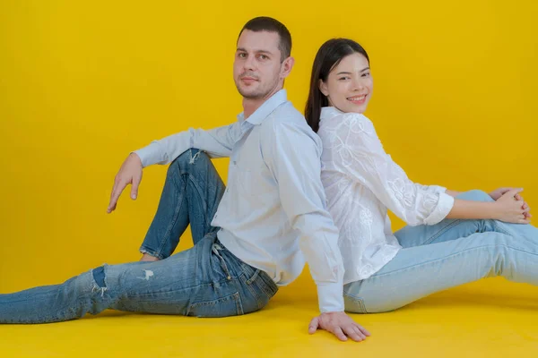 Couple Smiling Sitting Together Floor Looking Camera Yellow Background — Stock Photo, Image