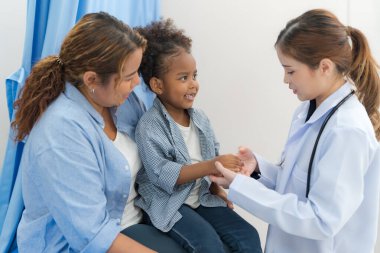 The girl sits on the patient's bed for the doctor to examine the body.