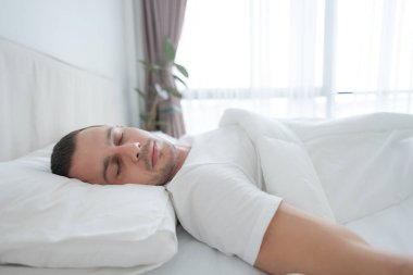Genç adam rahat bir beyaz yatak odasında uyudu. Bedeni dinlendir..